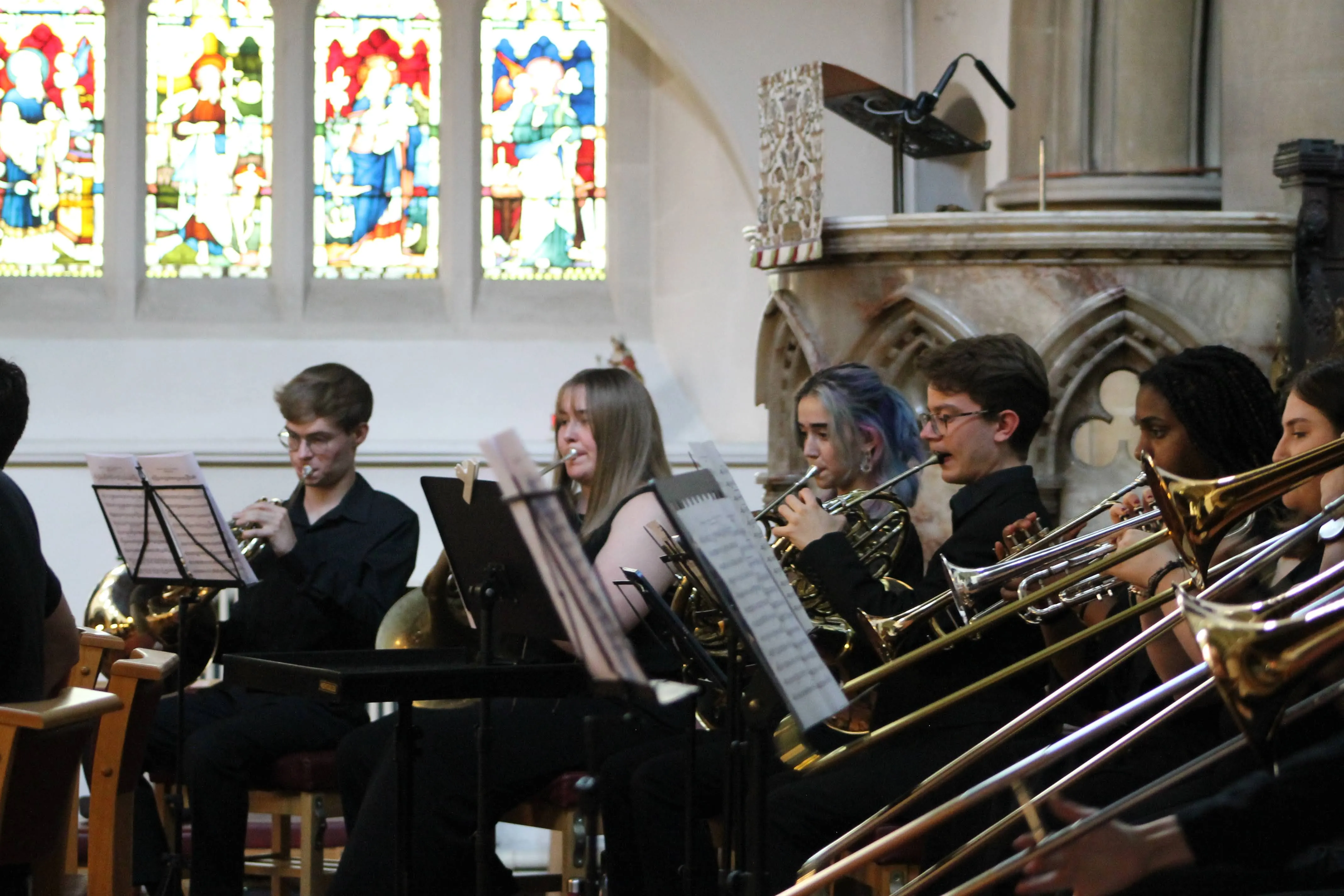 The brass section performing beneath the stained glass.