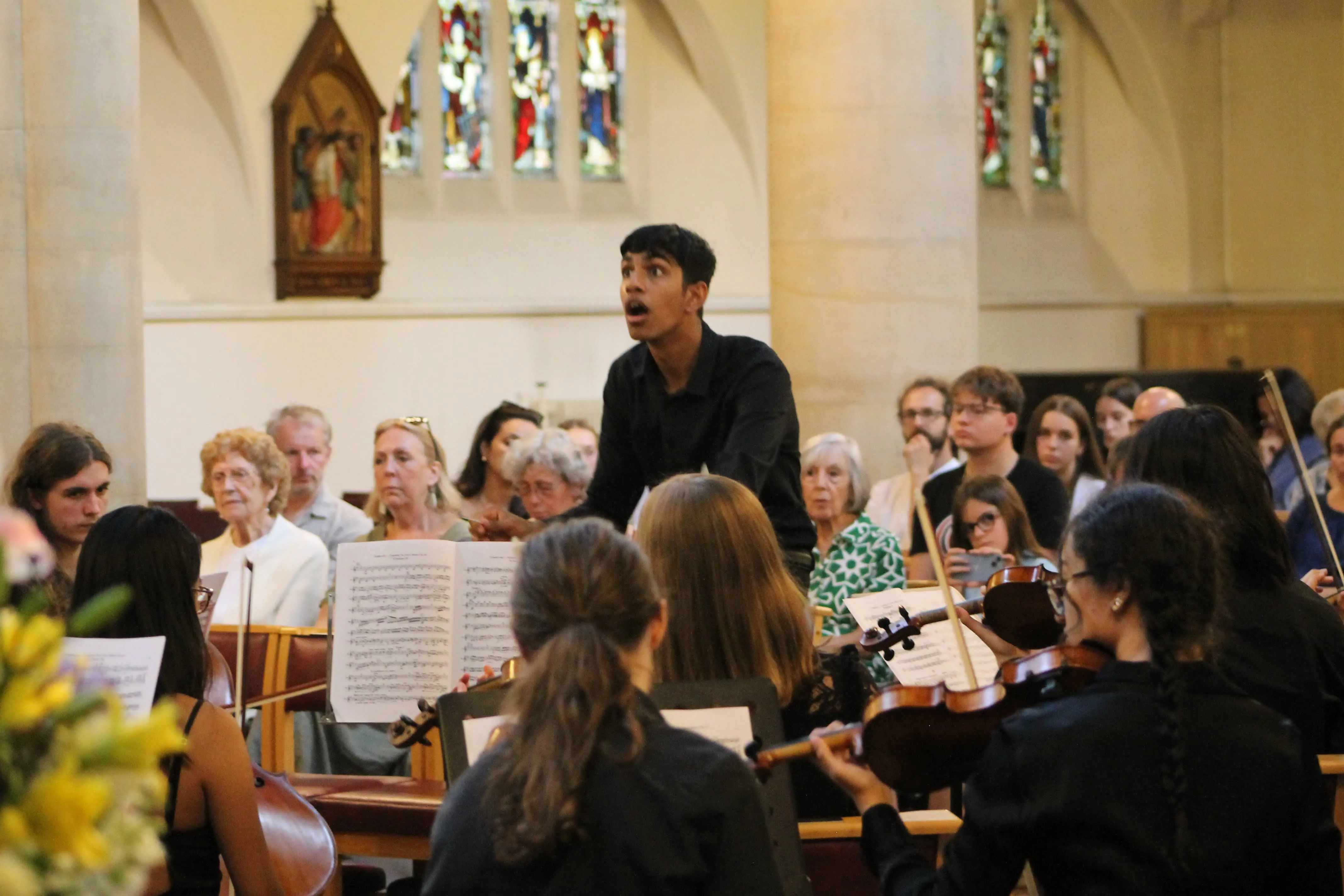 The conductor caught mid-cue before the stained-glass windows.